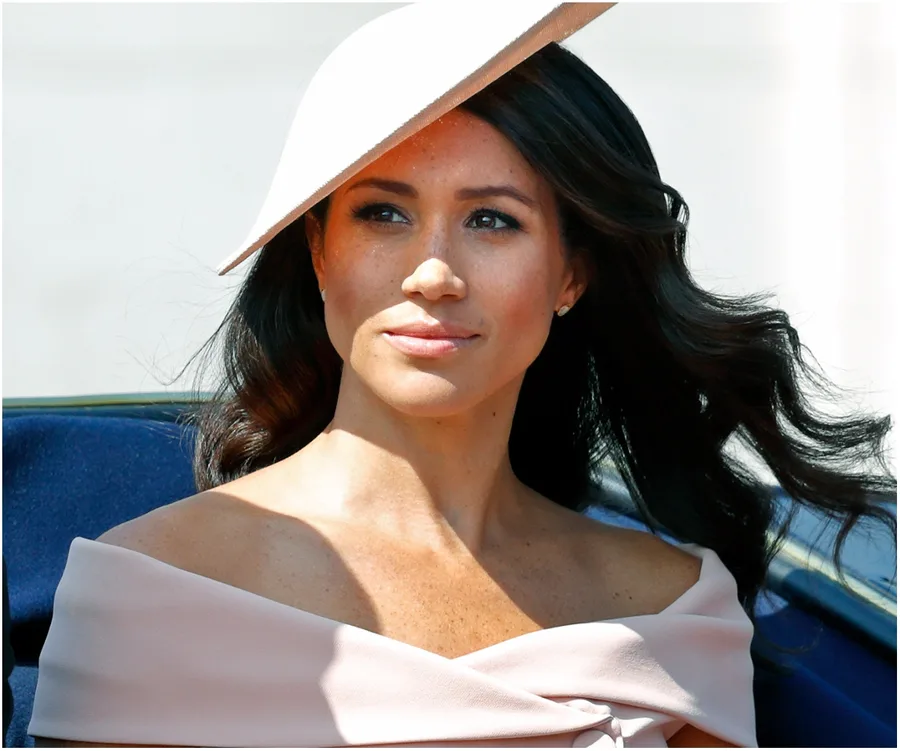 I don’t know who this is, but the image shows a person with long hair wearing an off-the-shoulder outfit and a hat outdoors.