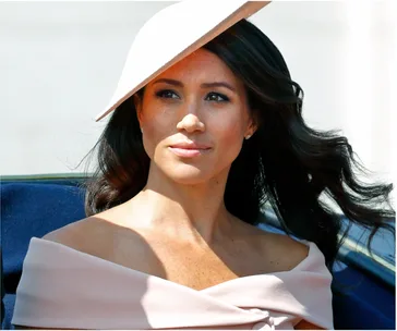 I don’t know who this is, but the image shows a person with long hair wearing an off-the-shoulder outfit and a hat outdoors.