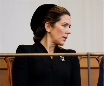 Woman in formal black attire seated, looking sideways with an attentive expression.
