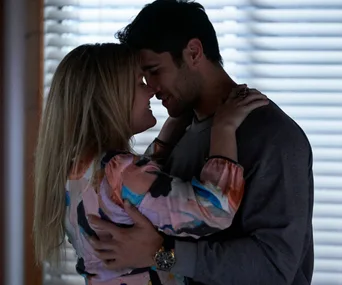 Ziggy and Tane embrace closely, smiling tenderly at each other in a warmly lit room.
