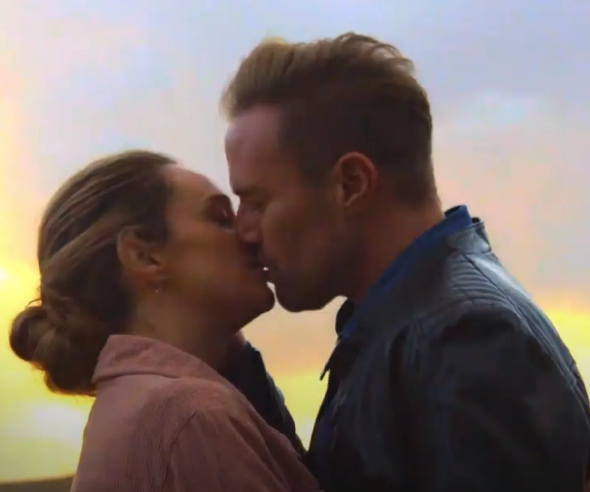 A couple sharing a kiss at sunset, with a warm glow in the background.
