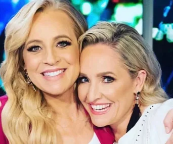 Two women smiling closely together, with one embracing the other. Bright background with colorful lights.
