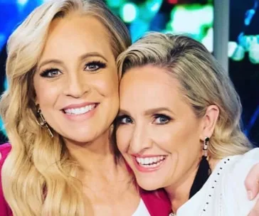 Two women smiling closely together, with one embracing the other. Bright background with colorful lights.