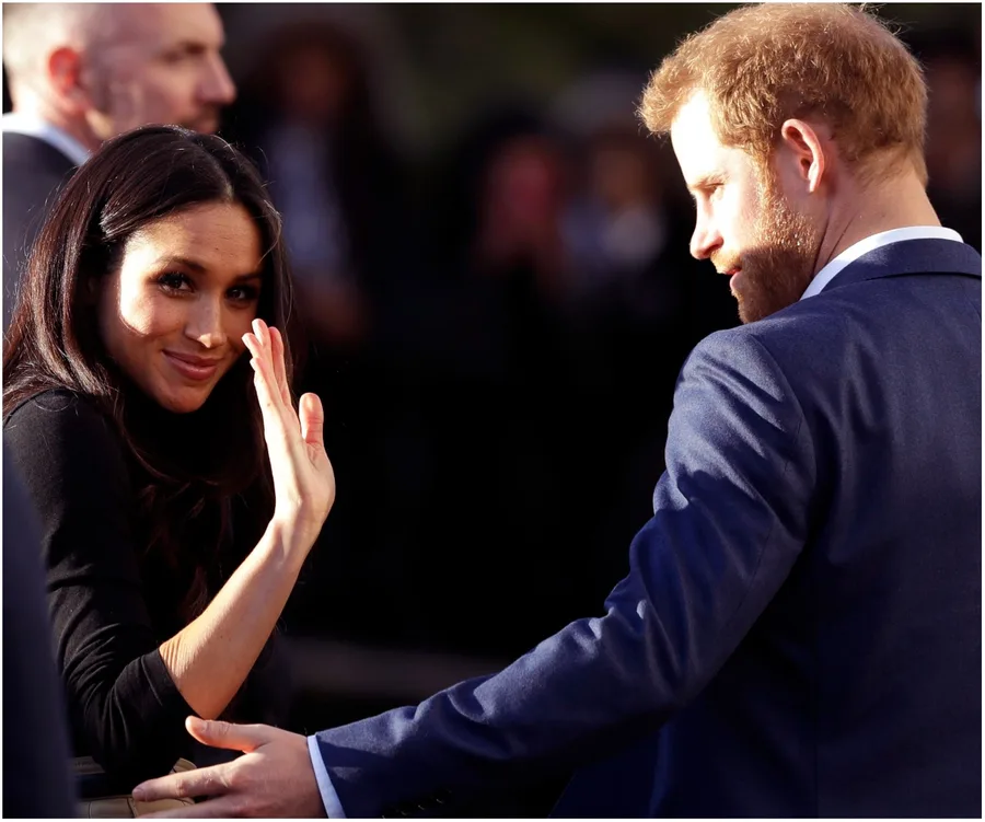 Couple smiling and waving at an outdoor event, surrounded by onlookers.
