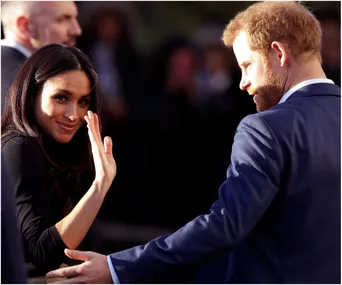 Couple smiling and waving at an outdoor event, surrounded by onlookers.