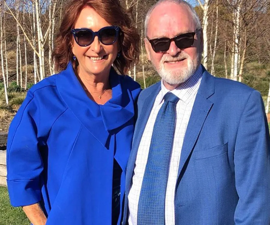 A couple dressed in matching blue outfits smiling outdoors in sunlight.