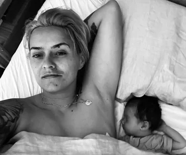 Person lying in bed next to a baby, both appearing peaceful and relaxed.