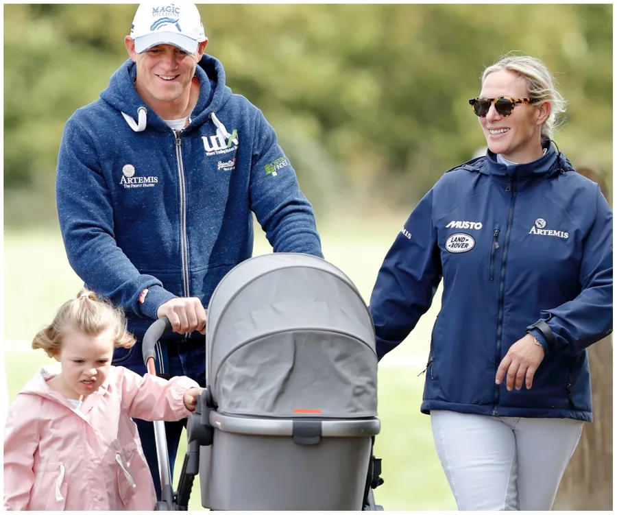 A smiling couple walks with a young child and a stroller in a park.