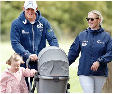 A smiling couple walks with a young child and a stroller in a park.