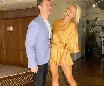 Man in light blue jacket and woman in gold dress laughing together indoors.