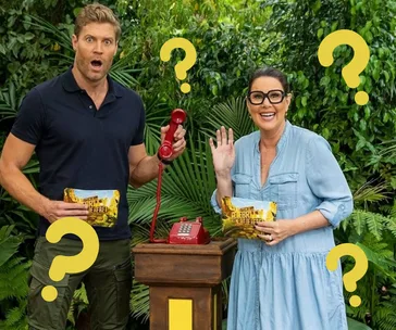 Two people in the jungle with question marks, holding a red phone and "I'm a Celebrity" clue cards.
