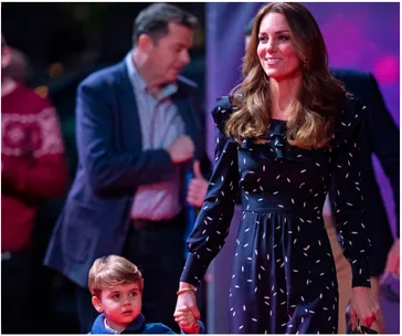 Woman in a navy Alessandra Rich dress holding a child's hand at an event, with blurred people in the background.