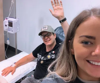 Man receiving treatment while smiling and waving, woman taking a selfie.