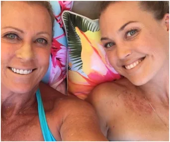 Two women smiling close-up, with colorful floral cushions in the background.