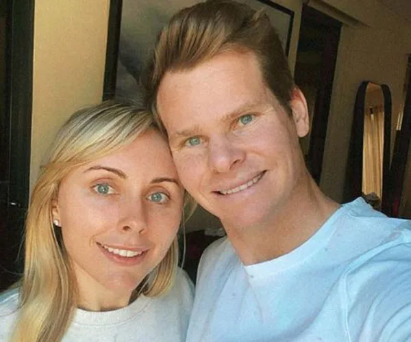 A couple smiling together in a warmly lit room, both wearing casual white tops.