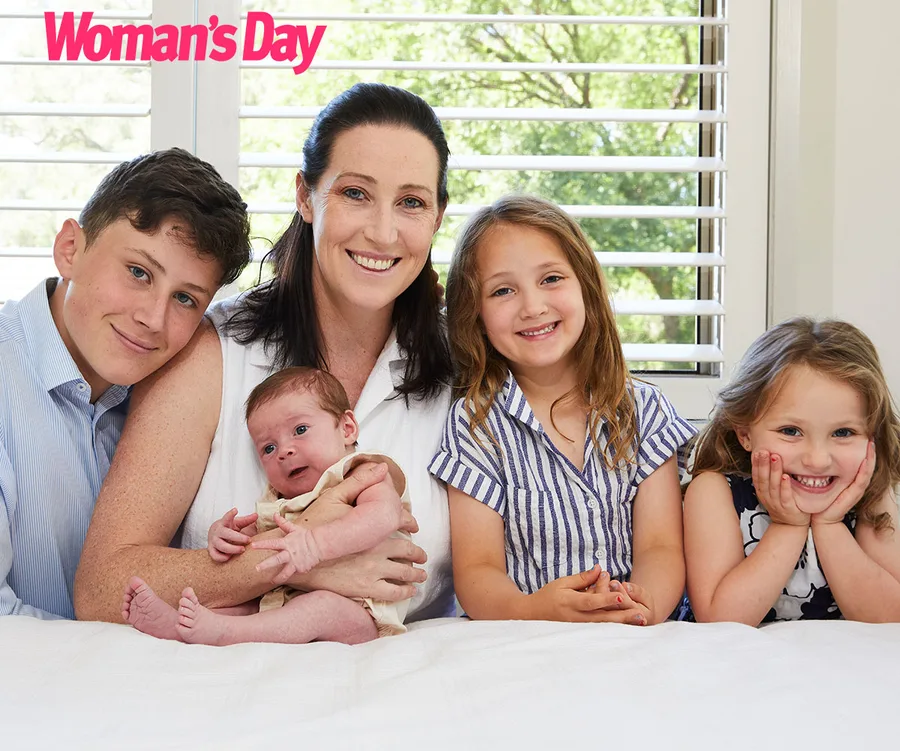 A woman and four children smile, sitting closely in a bright room, with "Woman's Day" logo above.