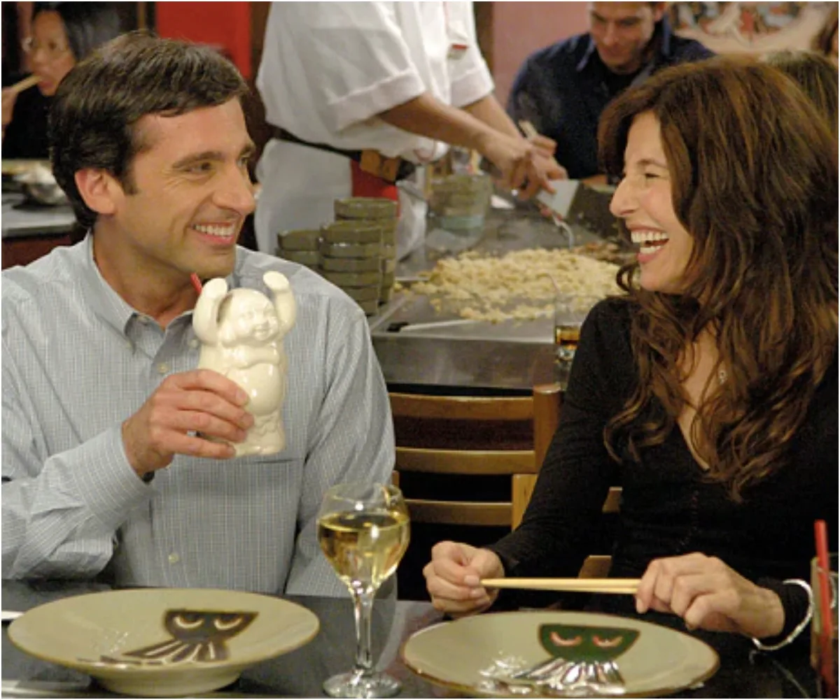 A man and woman sit at a restaurant table, smiling and laughing, with plates and drinks in front of them.
