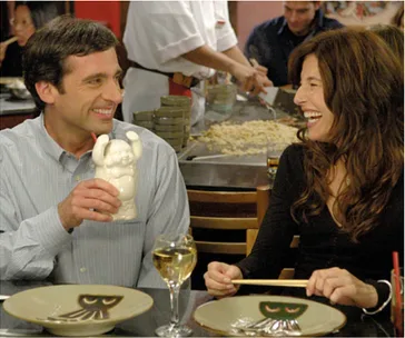 A man and woman sit at a restaurant table, smiling and laughing, with plates and drinks in front of them.