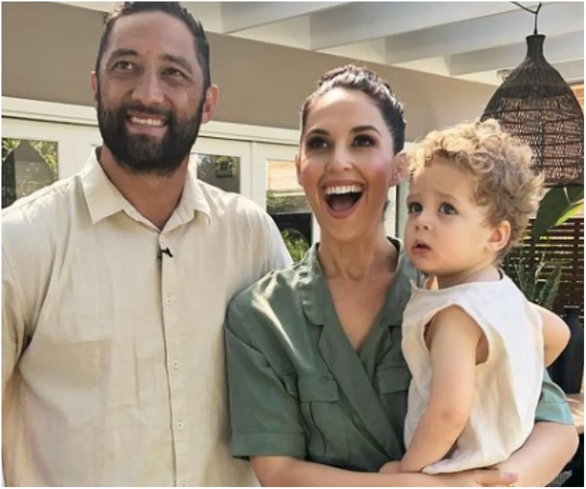 Family of three smiling outdoors, with one parent holding their young child.