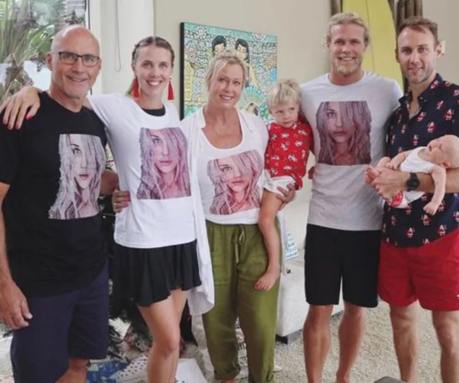 Family wearing matching shirts with a woman's face on them, posing together indoors with two young children.