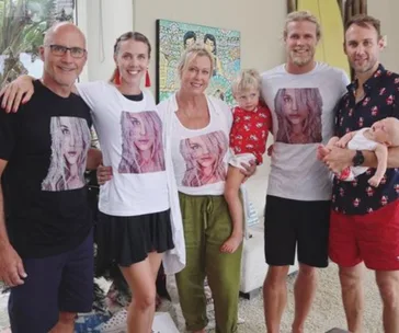 Family wearing matching shirts with a woman's face on them, posing together indoors with two young children.