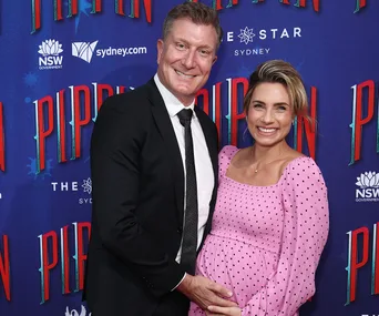 Couple smiling at a "Pippin" event; woman in pink dress, man in suit.