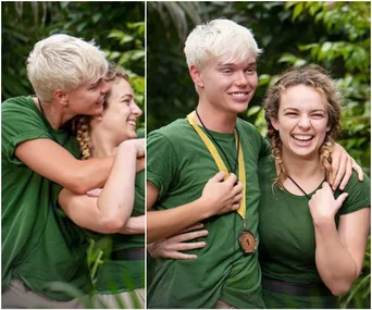 Two people in green shirts smiling and hugging in a lush outdoor setting; one wears a medal.