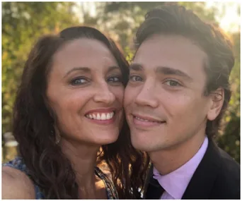 Two people smiling closely, outdoors with greenery in the background.