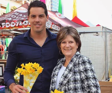Two people smiling at a market stall, holding a bouquet of yellow flowers.