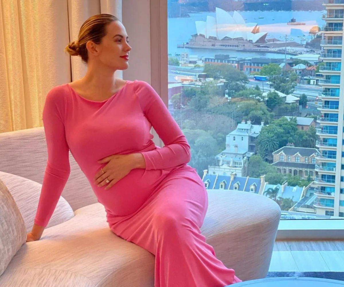 Pregnant woman in pink dress sitting by a window with Sydney Opera House in the background.