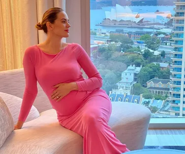 Pregnant woman in pink dress sitting by a window with Sydney Opera House in the background.