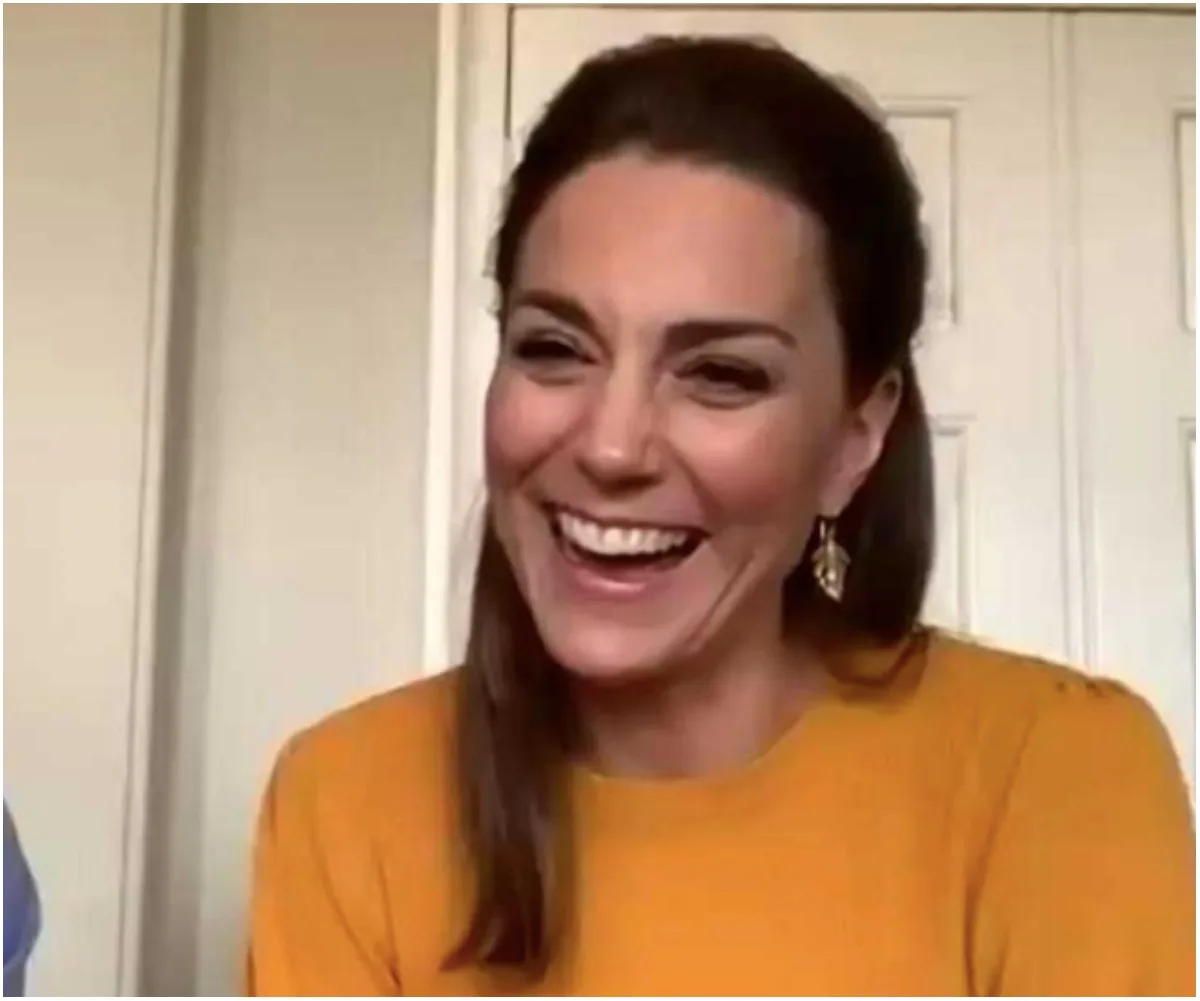 Smiling woman with long brown hair and yellow top, laughing warmly.