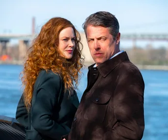 Two characters from "The Undoing" stand by a waterfront with a bridge in the background.