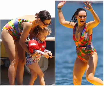 Woman in a colorful swimsuit playing with a child in a life jacket at the beach.