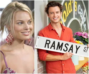 Two people smiling; one holding a "Ramsay St" sign, likely related to the TV show "Neighbours."