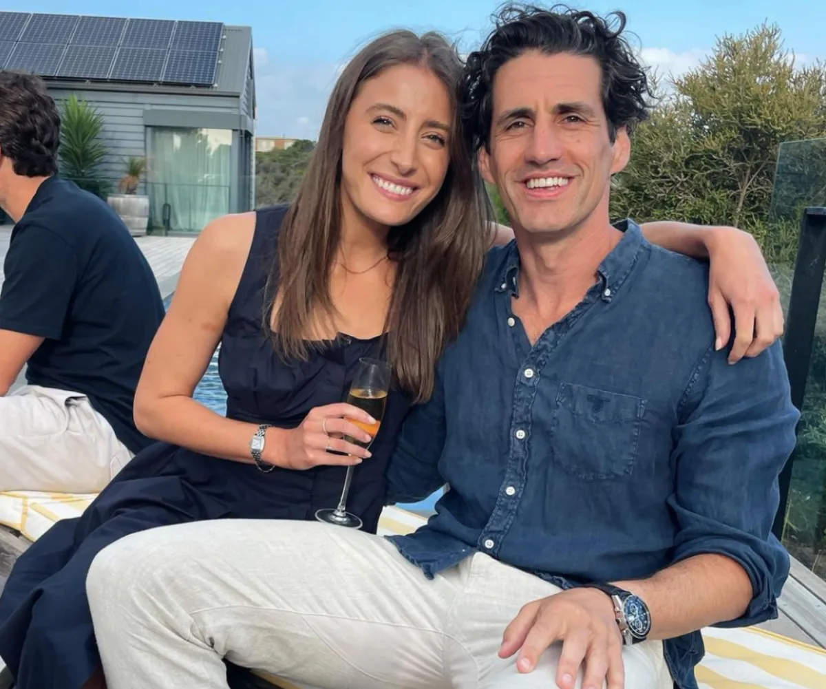 Couple sitting close together, smiling, with the woman holding a champagne glass outdoors.