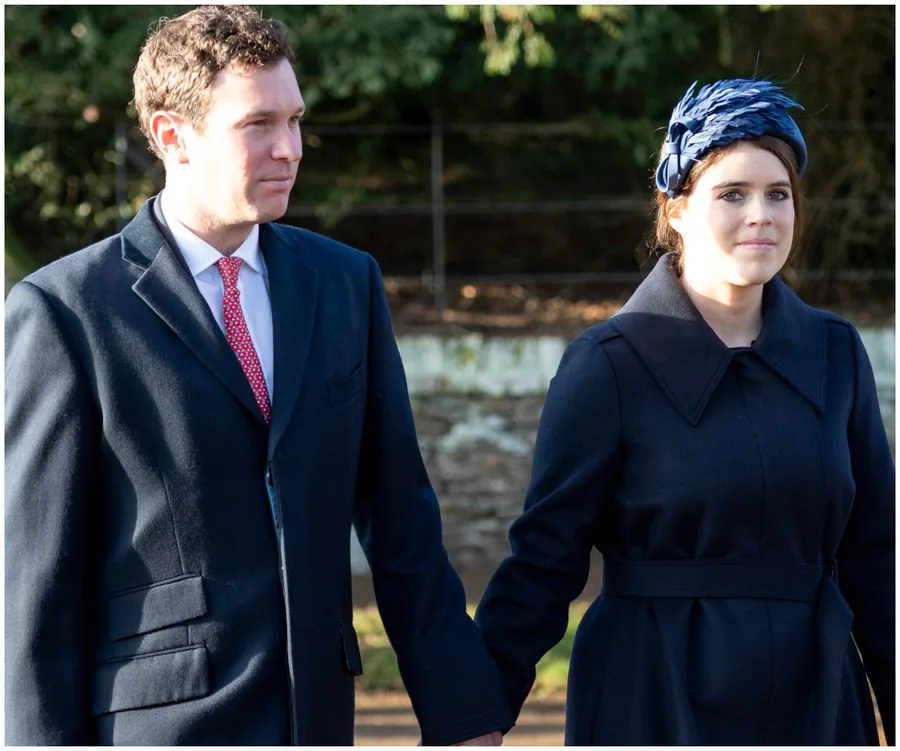 A couple holding hands outdoors, both wearing dark coats; the woman has a blue hat with feathers.