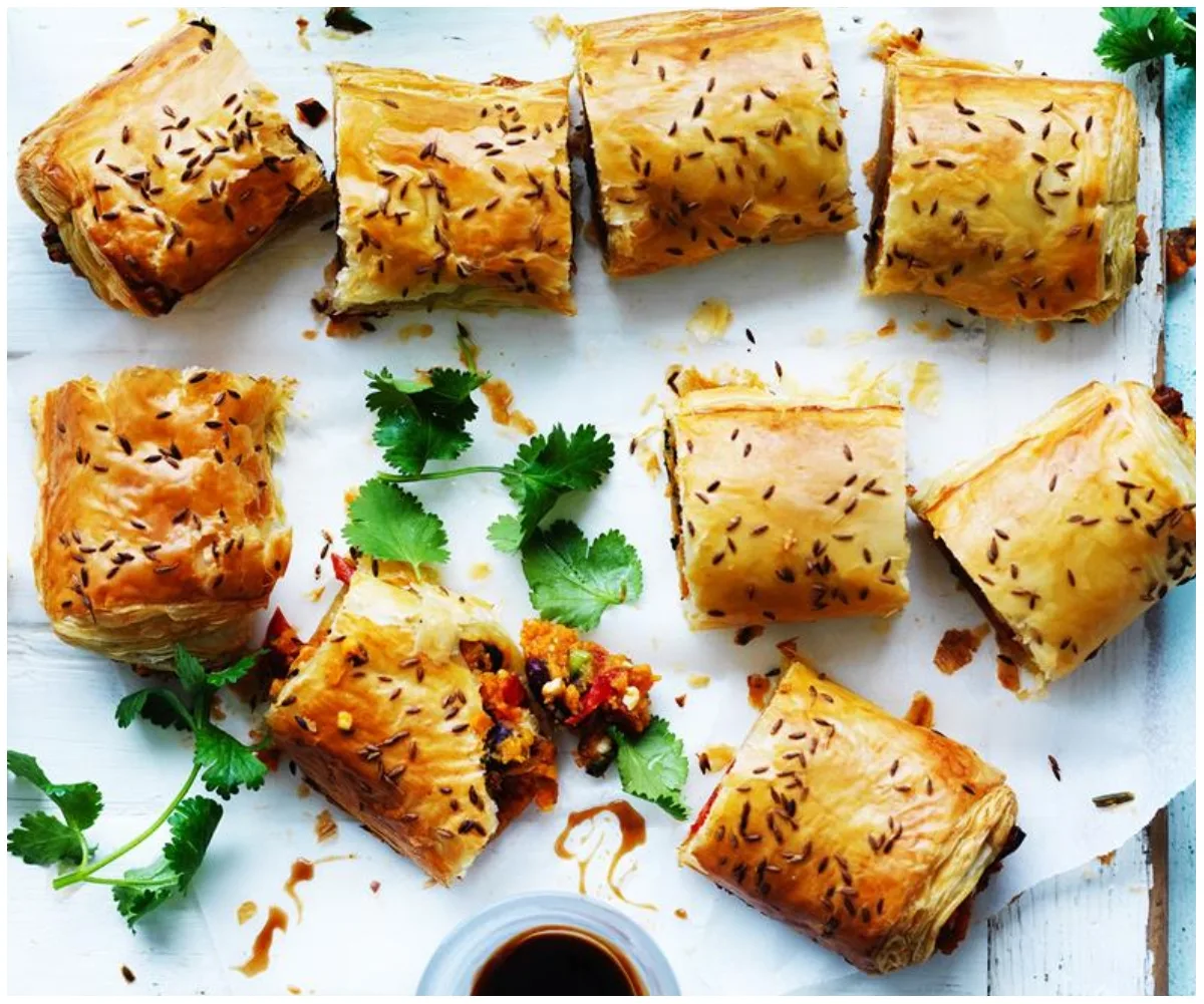 Golden-brown sausage rolls sprinkled with seeds, garnished with fresh cilantro on a white surface.