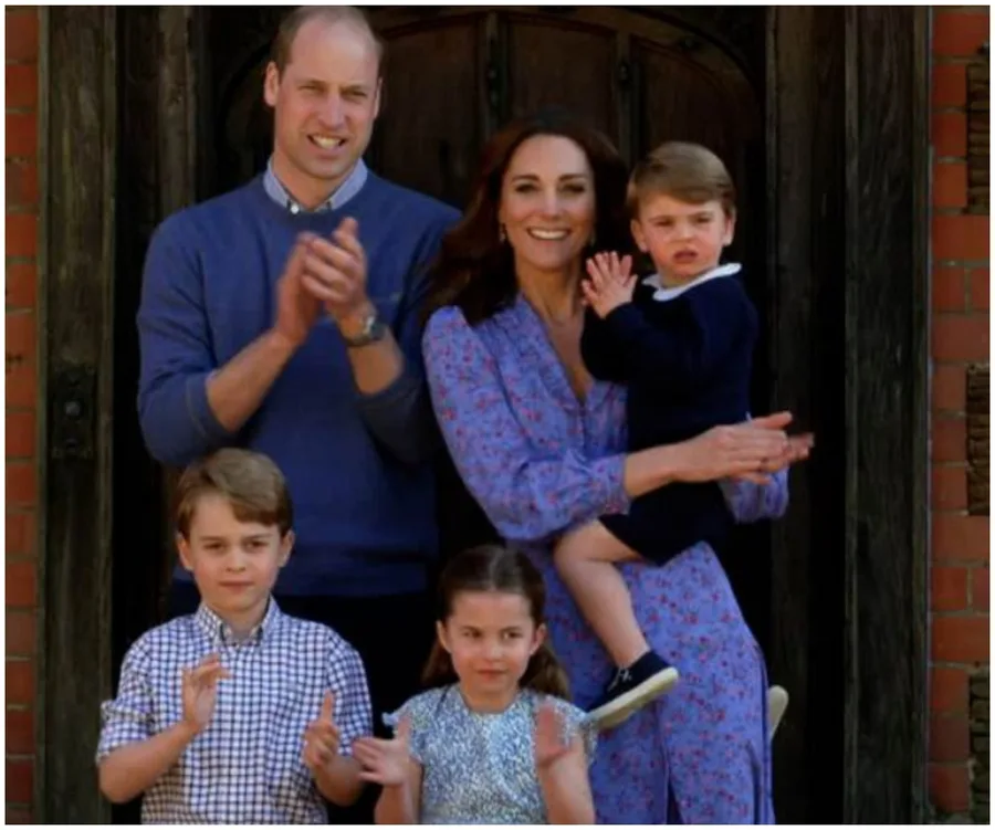 A family of five clapping outside, with parents in back, children in front; the mother holds the youngest child.