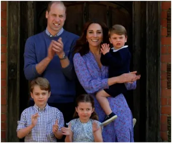 A family of five clapping outside, with parents in back, children in front; the mother holds the youngest child.