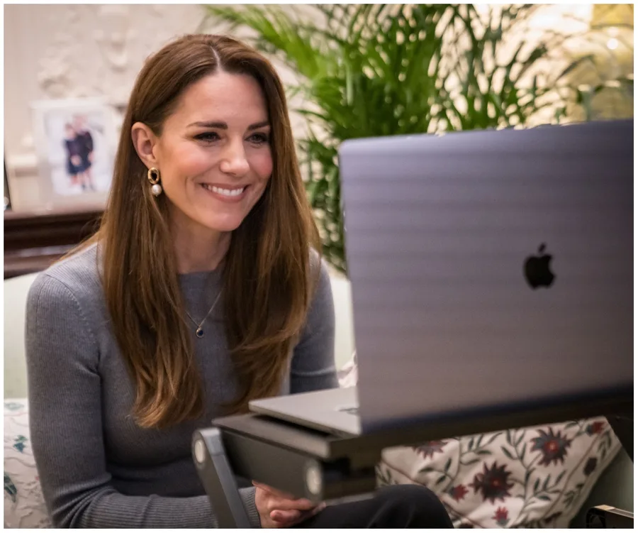 Kate Middleton smiling during a video call, seated indoors with a laptop.