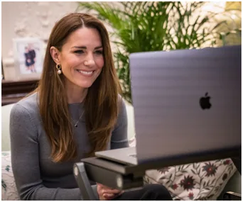 Kate Middleton smiling during a video call, seated indoors with a laptop.