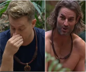 Two contestants from "I'm a Celebrity" in the jungle, one with hand on nose, the other shirtless and speaking.