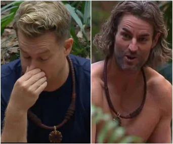 Two contestants from "I'm a Celebrity" in the jungle, one with hand on nose, the other shirtless and speaking.
