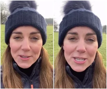 A woman outdoors wearing a navy knit hat with a pom-pom, speaking in a video message.