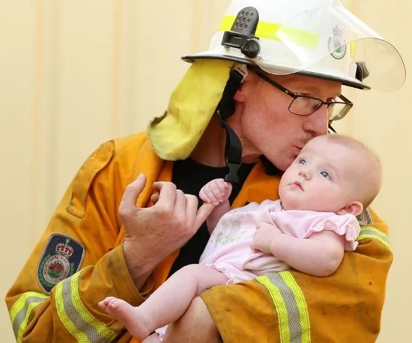 Firefighter in uniform kisses a baby while holding them in his arms, showing tenderness and care.