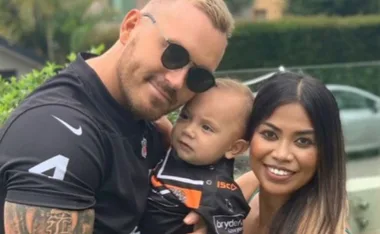 A family photo of a man, woman, and child outdoors, with the man wearing sunglasses and a sports jersey.