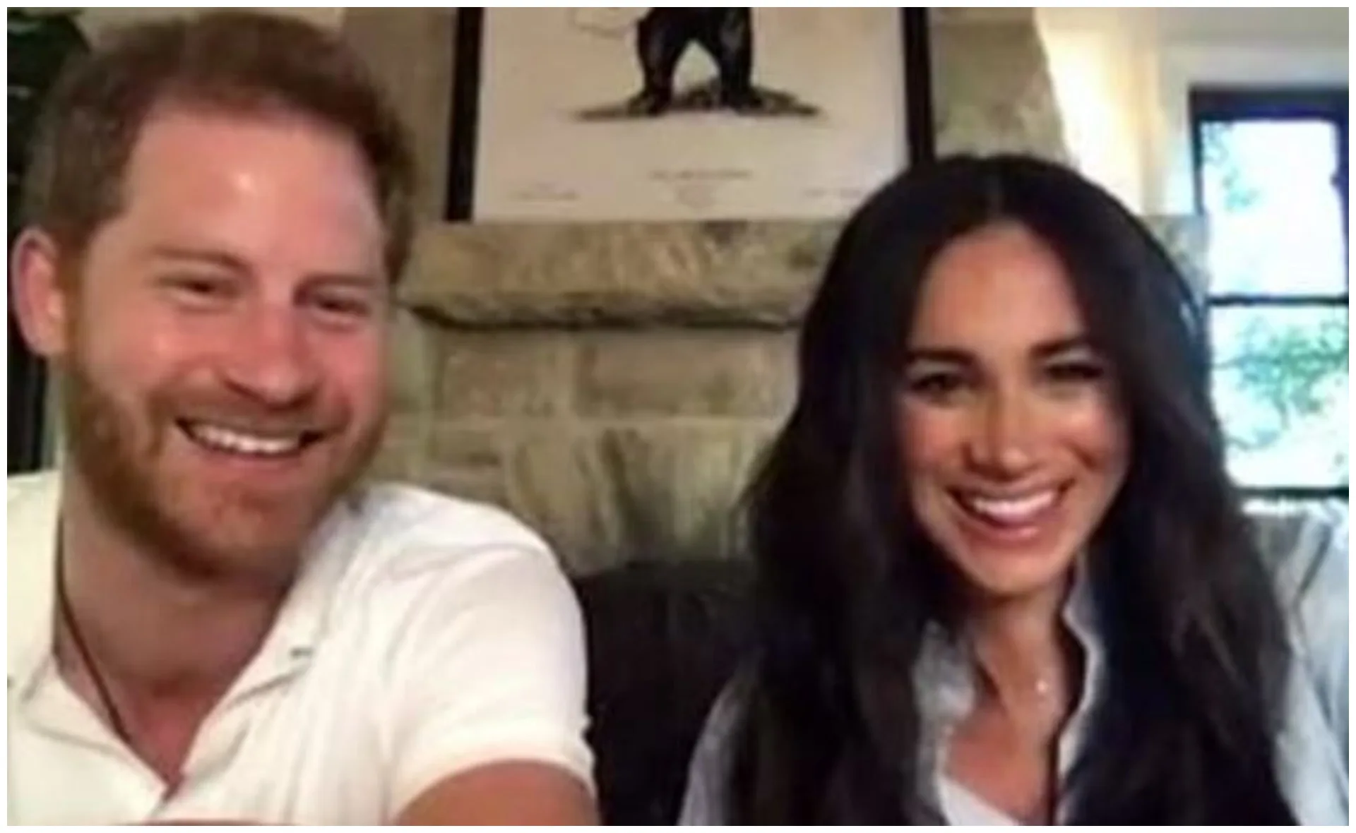 A smiling couple doing a video call from a cozy room with a stone fireplace and artwork in the background.
