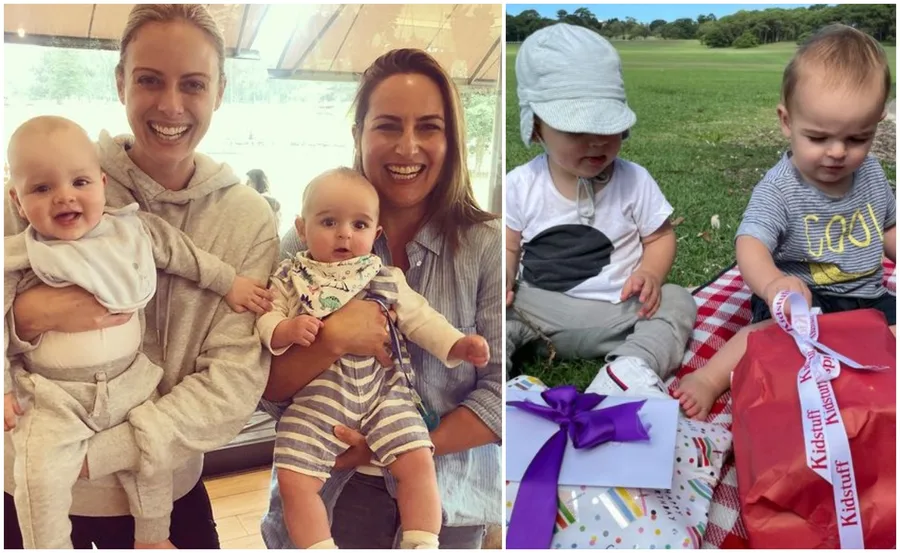 Two women smiling, each holding a baby, and two toddlers sitting on a picnic blanket with gifts.