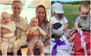 Two women smiling, each holding a baby, and two toddlers sitting on a picnic blanket with gifts.